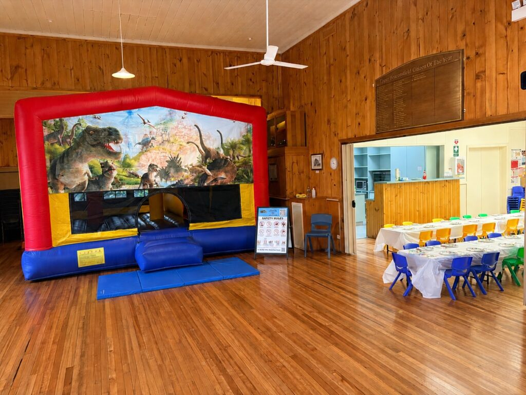 Dinosaur Adventure Combo jumping castle set up indoors at Upper Beaconsfield Community Hall for a children's birthday party.